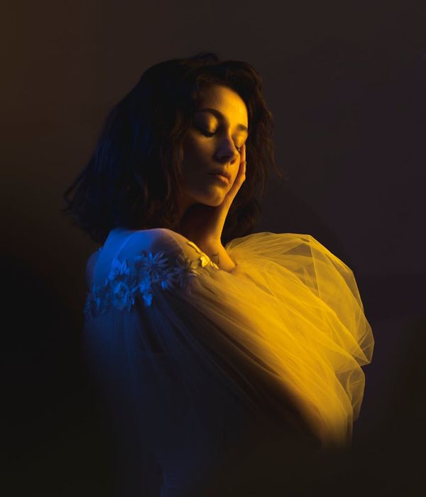 Woman in a serene yoga pose in a dark studio with cyan light.